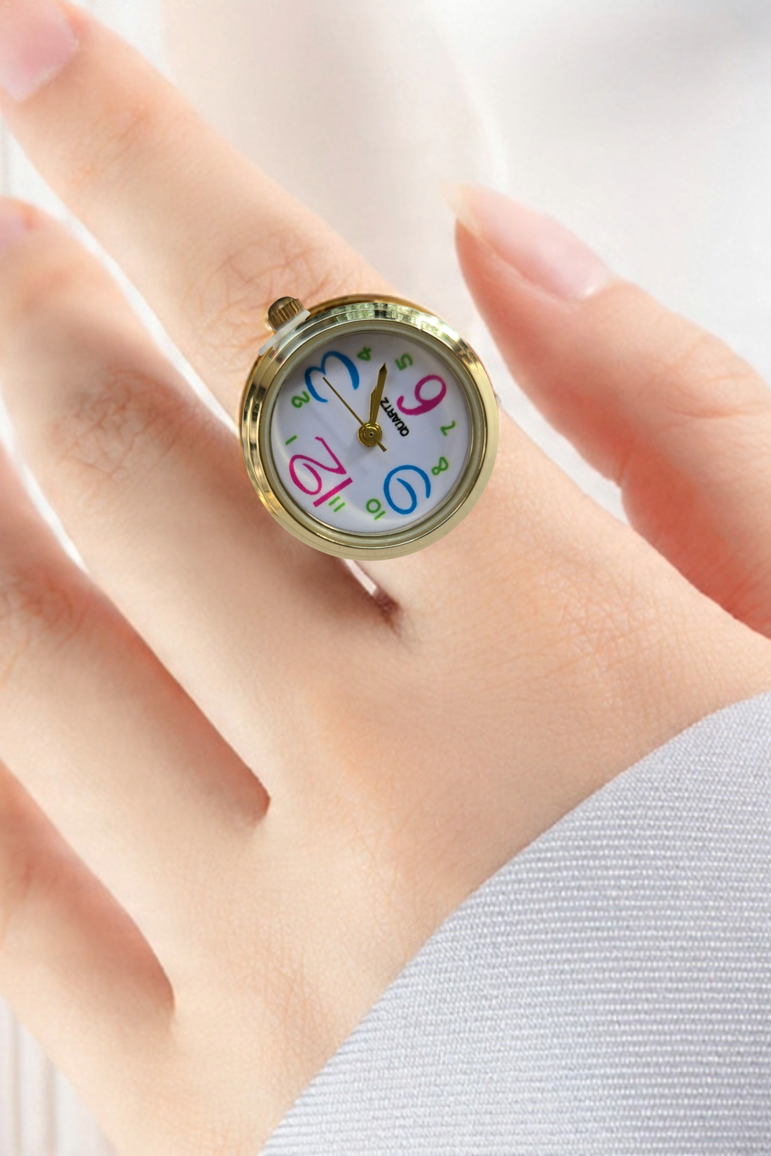 Close-up of a gold ring-style wristwatch on a finger, featuring a colorful numbers dial on a white face.
