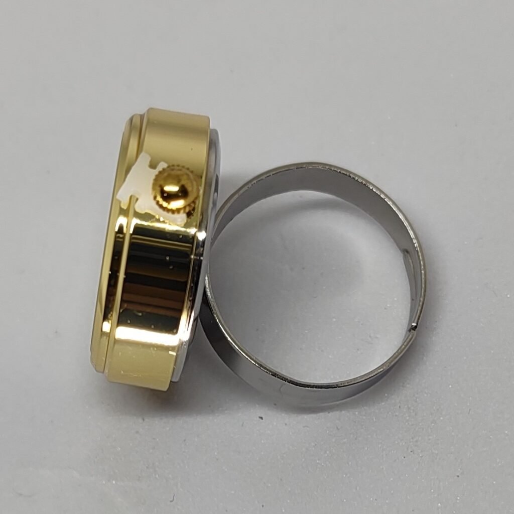 Close-up of two interlocking metal rings: a gold-tone ring with a small knurled adjustment knob and a silver ring beside it, with a white spacer visible.